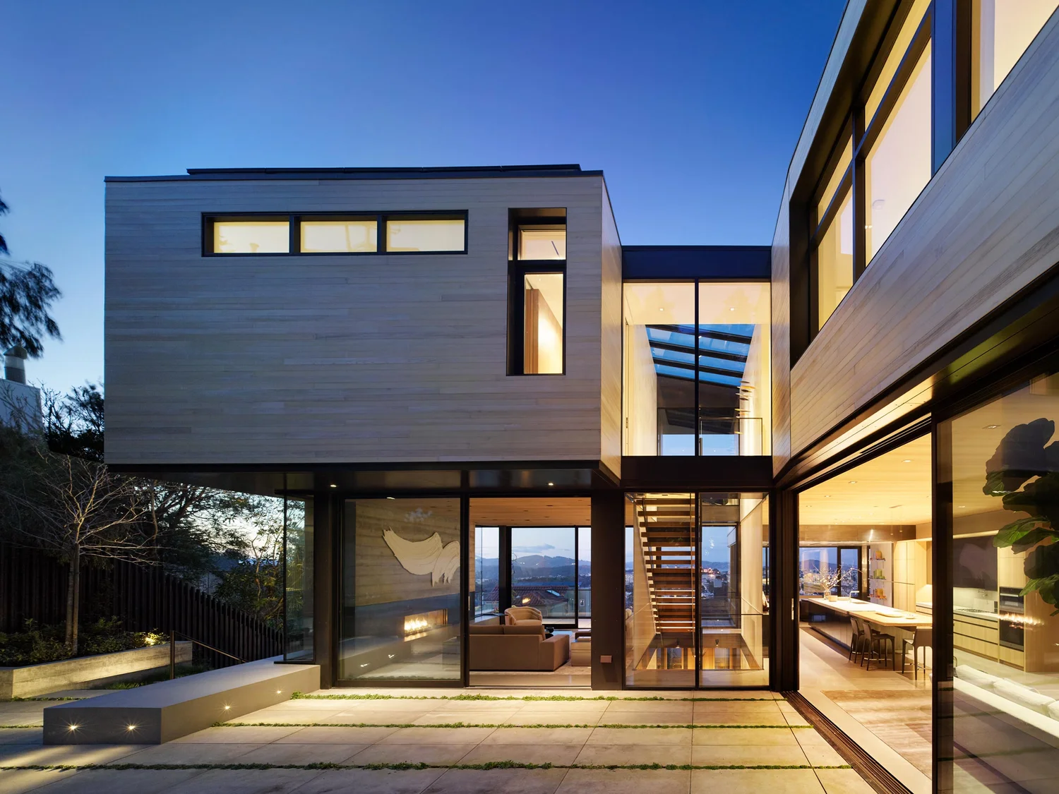 A Hughes-built contemporary home illuminated at dusk, with an open courtyard and floor-to-ceiling glazing